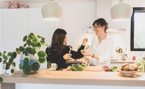 mère et fille qui cuisinent ensemble en souriant dans une cuisine lumineuse avec légumes frais, kiwis et plantes vertes