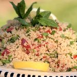 plat de taboulet d'été au citron et menthe fraiche servi dans un grand plat artisanal rayé, avec tomates et herbes