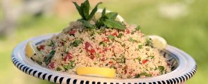 plat de taboulet d'été au citron et menthe fraiche servi dans un grand plat artisanal rayé, avec tomates et herbes