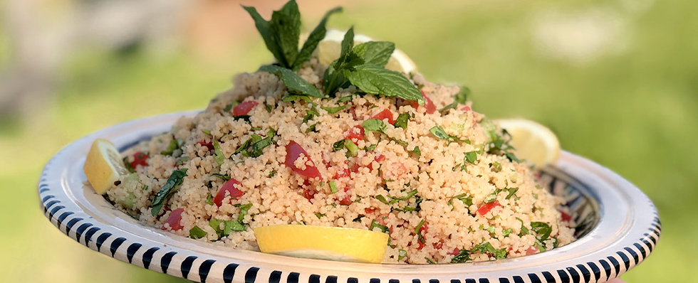 plat de taboulet d'été au citron et menthe fraiche servi dans un grand plat artisanal rayé, avec tomates et herbes