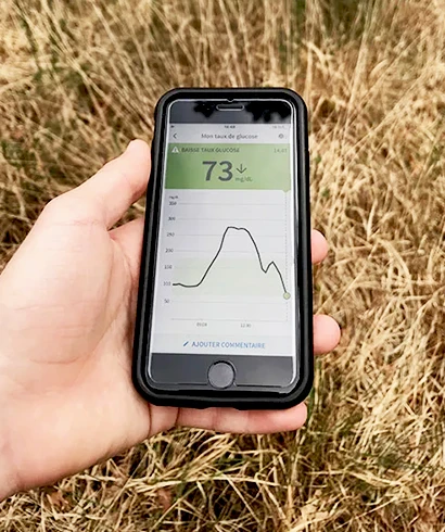 Main tenant un smartphone affichant 73 mg/dl avec courbe de glycémie et alerte basse taux de glucose dans un champ