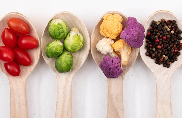 Quatre cuillères en bois avec légumes à IG bas : tomates cerises, choux de Bruxelles, choux-fleurs colorés et grains de poivre