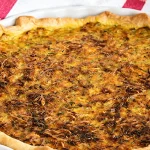 tarte aux légumes maison dorée dans son plat blanc posée sur un torchon à rayures rouges et jaunes