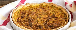 tarte aux légumes maison dorée dans son plat blanc posée sur un torchon à rayures rouges et jaunes