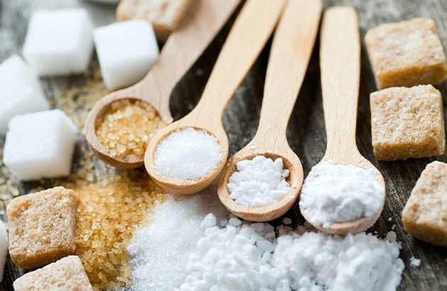Quatre cuillères en bois avec différents sucres dont dextrose, sucre blanc et cassonade, avec morceaux de sucre